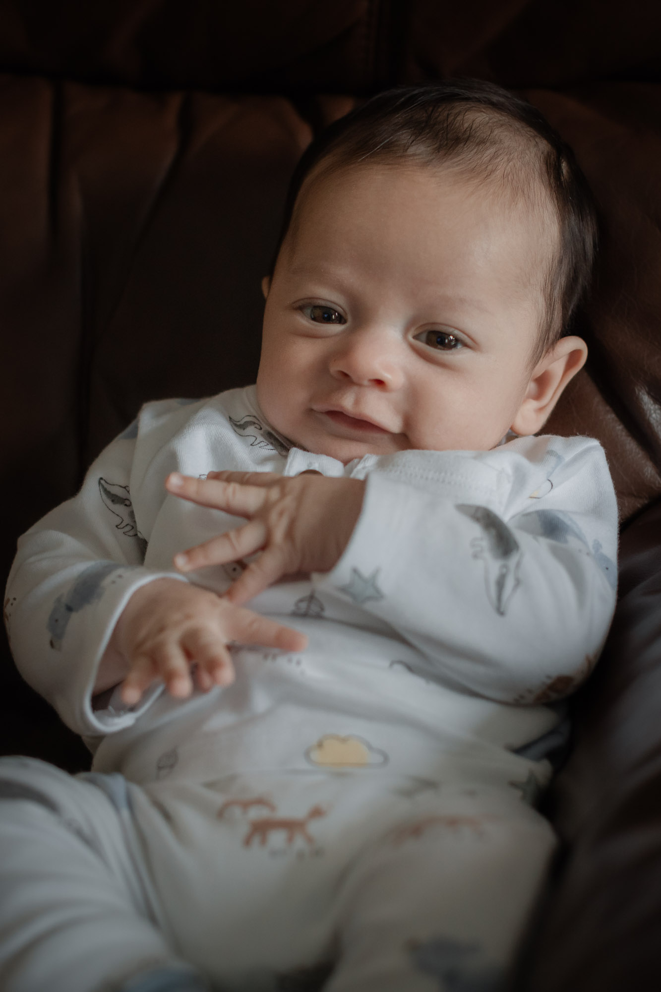 A baby boy looking at the camera while propped up on a sofa in a newborn photoshoot in Horsham West Sussex.