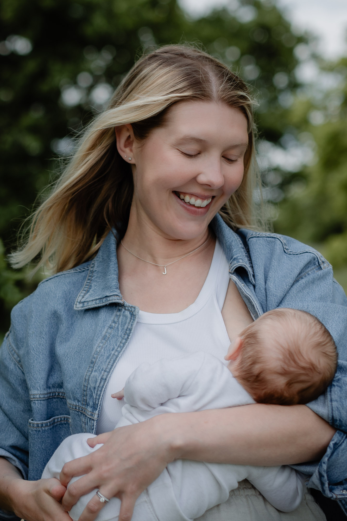 A young mother cradling her baby and smiling while looking down at him on a newborn photoshoot in Horsham West Sussex